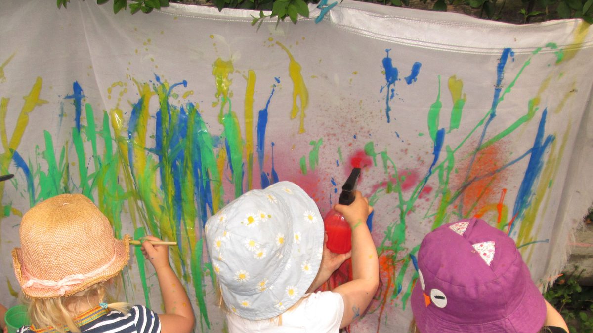 Children painting a big outdoor canvas with brushes and spray bottles